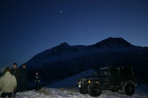 2003 Jeep TJ - A black Jeep Wrangler is parked in a snowy mountain landscape under a twilight sky with a crescent moon visible.