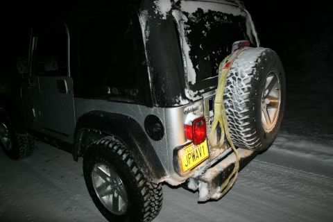 2003 Jeep TJ - A silver Jeep Wrangler is parked on a snowy road at night, with snow covering its exterior.
