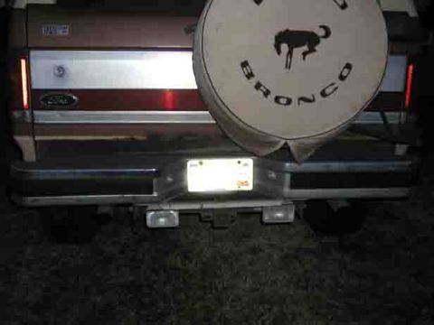 1988 Ford Bronco - The rear of a 1988 Ford Bronco is visible, its spare tire cover with the iconic Bronco emblem.