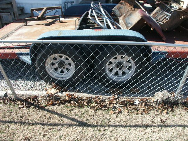 Trailer with two wheels, metal deck, and various scrap metal parts piled on top. Chain-link fence in foreground