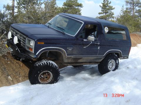 2000 Ford F-450 - A dark blue Ford Bronco navigates a snowy, off-road trail with large tires.