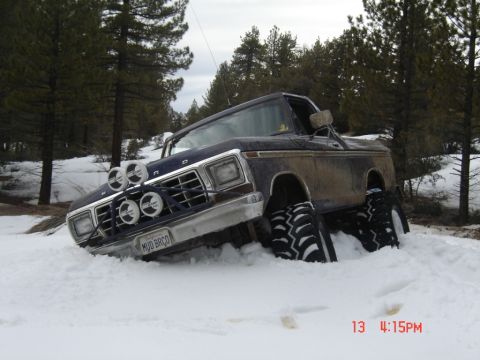 2000 Ford F-450 - This Ford F-Series truck, likely from the 1970s, is deeply stuck in snow with its large off-road tires buried.