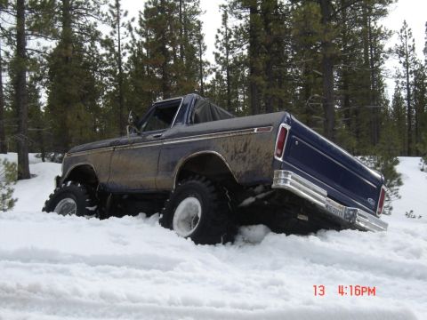 2000 Ford F-450 - A mud-splattered dark blue late-1970s Ford pickup with a chopped/soft-top cab, chrome side trim and rear bumper sits axle-deep in packed sn…