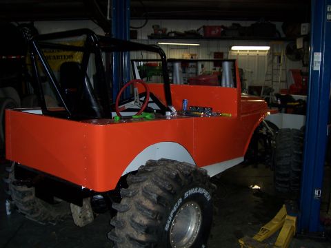 1999 Jeep TJ - This heavily modified Jeep-like vehicle is undergoing work in a garage, oversized tires and a custom orange body.