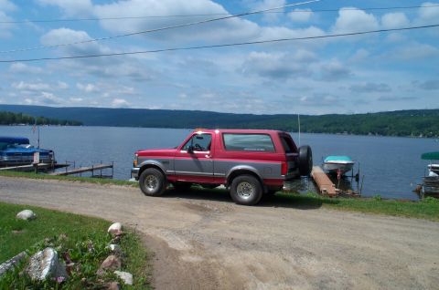 1995 Ford Bronco - A red and grey Ford Bronco is parked by a lake with a spare tire on the back.