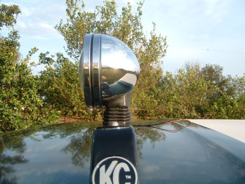 1993 Ford Bronco - A close-up of a KC light mounted on the roof of a vehicle, with a reflection of the surroundings visible on the chrome housing.