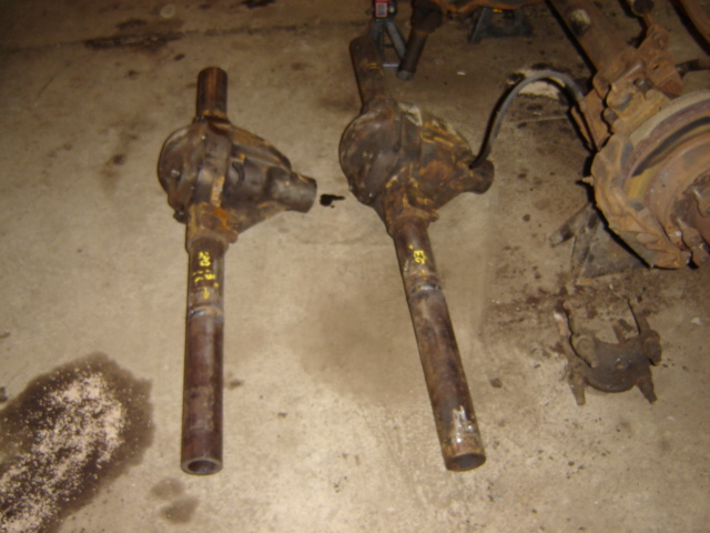 Two rusty differential assemblies sit on a concrete floor. Yellow markings are visible on the tubes