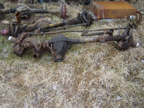 1992 Ford Bronco - Multiple vehicle axles are shown resting on dry grass, suggesting they are parts for sale or salvage.