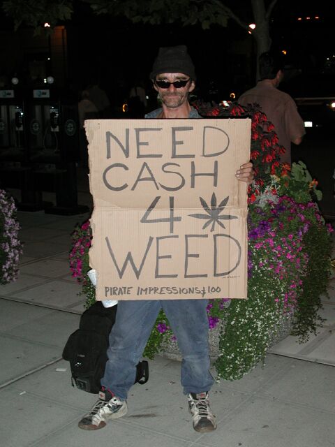 1991 Ford Bronco - A person holds a cardboard sign asking for cash for weed, with "PIRATE IMPRESSIONS" and "100" written at the bottom.