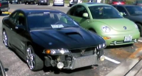 2000 Ford Crown Victoria - A modified black coupe is parked next to a green Volkswagen Beetle.
