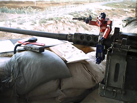 1990 Ford Bronco - Optimus Prime toy positioned on a heavy machine gun, set against a backdrop of sandbags and a fence.