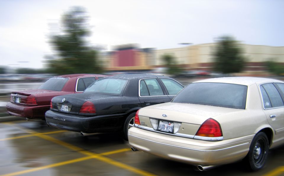 Three Ford Crown Victoria sedans parked at angles in a wet lot, tan, black and maroon