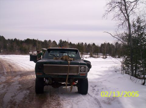 1978 Chevrolet C/K Pickup - A dark green pickup truck is parked on a snowy road with trees in the background.