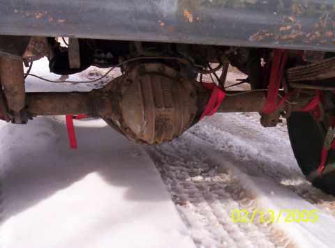 1978 Chevrolet C/K Pickup - Close-up of a vehicle's rear axle and suspension components, with red straps visible, on a snowy surface.