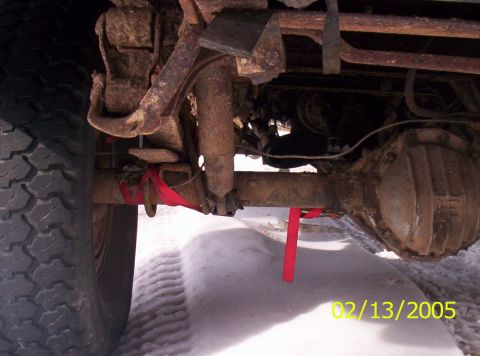 1978 Chevrolet C/K Pickup - Undercarriage view of a rusty rear axle with red straps and a tire in the snow.