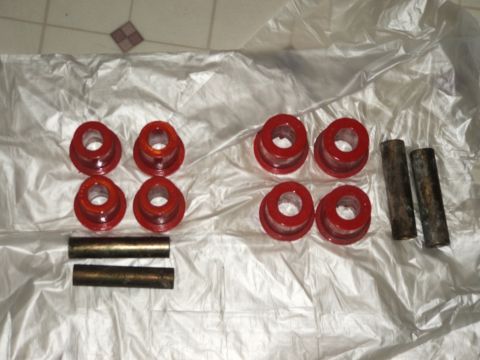 1991 Ford Bronco - Several red polyurethane bushings and two metal sleeves are displayed on a white plastic sheet.