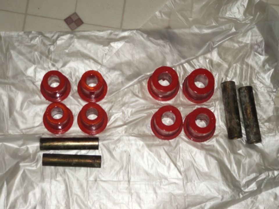 Red polyurethane suspension bushings and steel inner sleeves laid out on plastic sheeting
