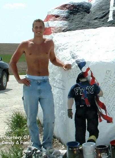 1991 Ford Bronco - A man poses next to a large rock painted with the American flag, with a mannequin dressed as a firefighter nearby.