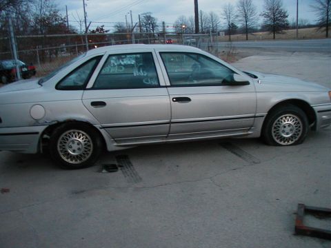 1997 Ford Taurus - A silver sedan sits with a flat tire and visible damage to the rear fender.