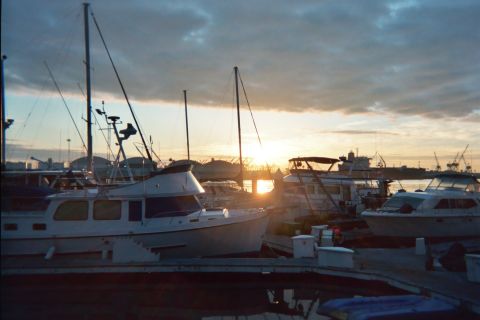 1990 Ford Bronco - sun sets over a marina of moored boats with harbor cranes silhouetted on the horizon.