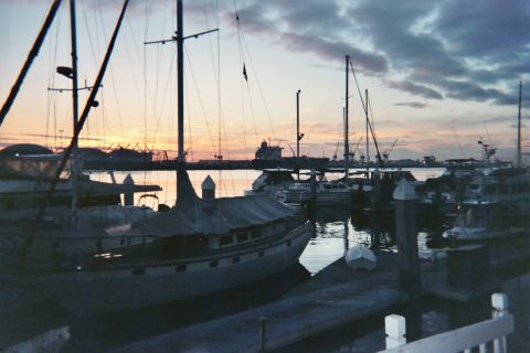 1990 Ford Bronco - Sailboat masts and yachts are silhouetted against an orange-and-blue dusk sky over a marina.