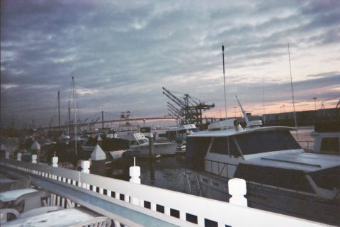 1990 Ford Bronco - Boats and harbor cranes sit under a grey dusk sky, viewed past a white railing with lit posts.