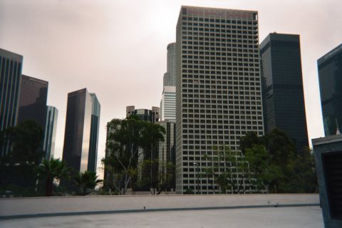 1990 Ford Bronco - Cluster of downtown office skyscrapers, dominated by a tall dark grid-windowed tower, under grey sky.