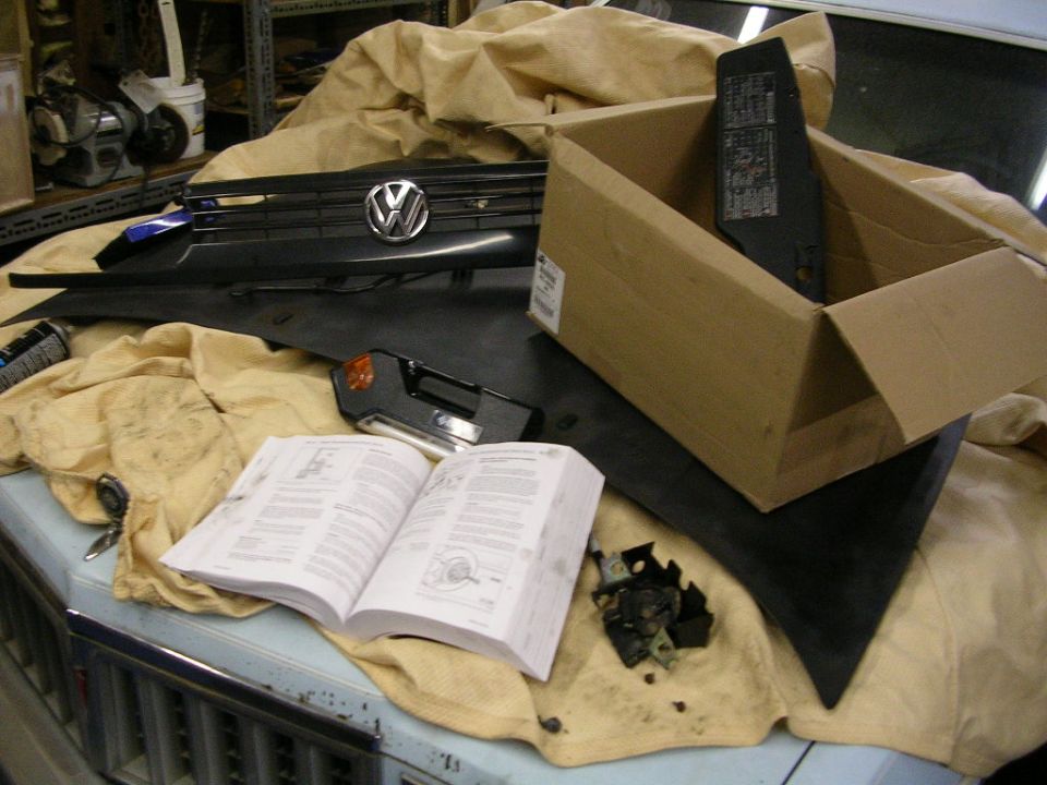 Volkswagen grille, fuse panel cover and open repair manual laid out on a hood