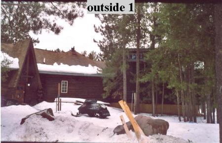 1995 Ford Bronco - A snowmobile sits in the snow outside a rustic log cabin, with trees and a second-story deck visible.