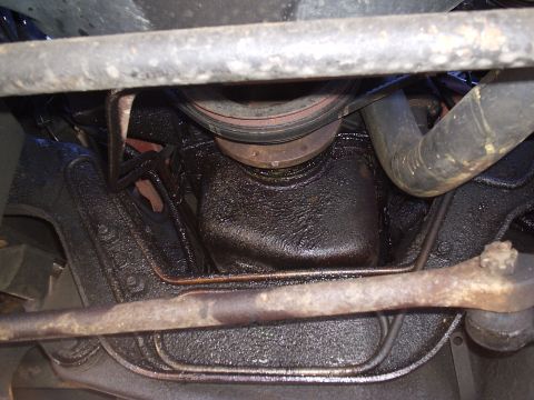 1985 Ford Bronco - The underside of a vehicle reveals an oily engine oil pan and corroded suspension components.