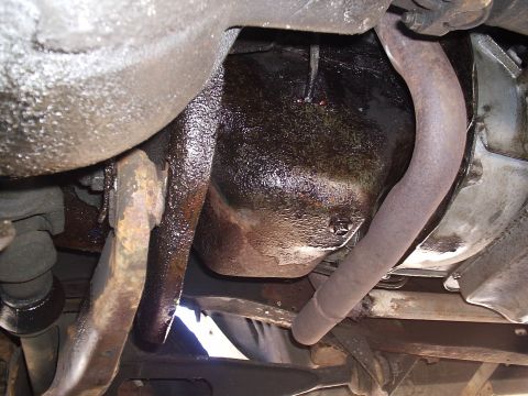 1985 Ford Bronco - Underside view of a vehicle's engine pan and exhaust pipe, showing oil accumulation.