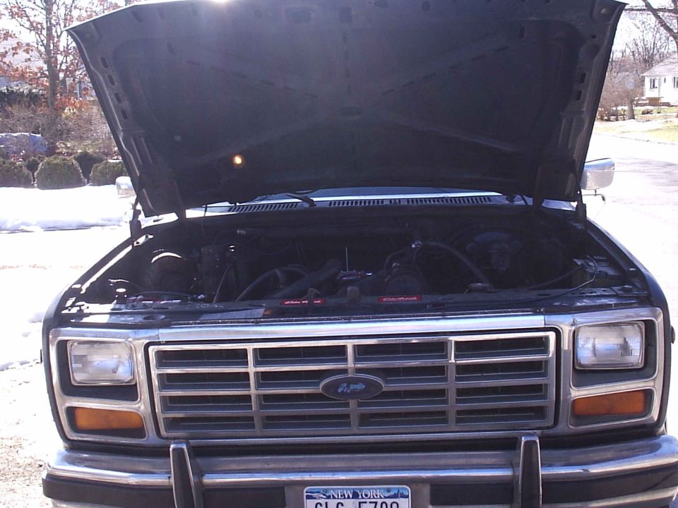 Front view of a dark-colored Ford Bronco with hood open, showing engine and grille