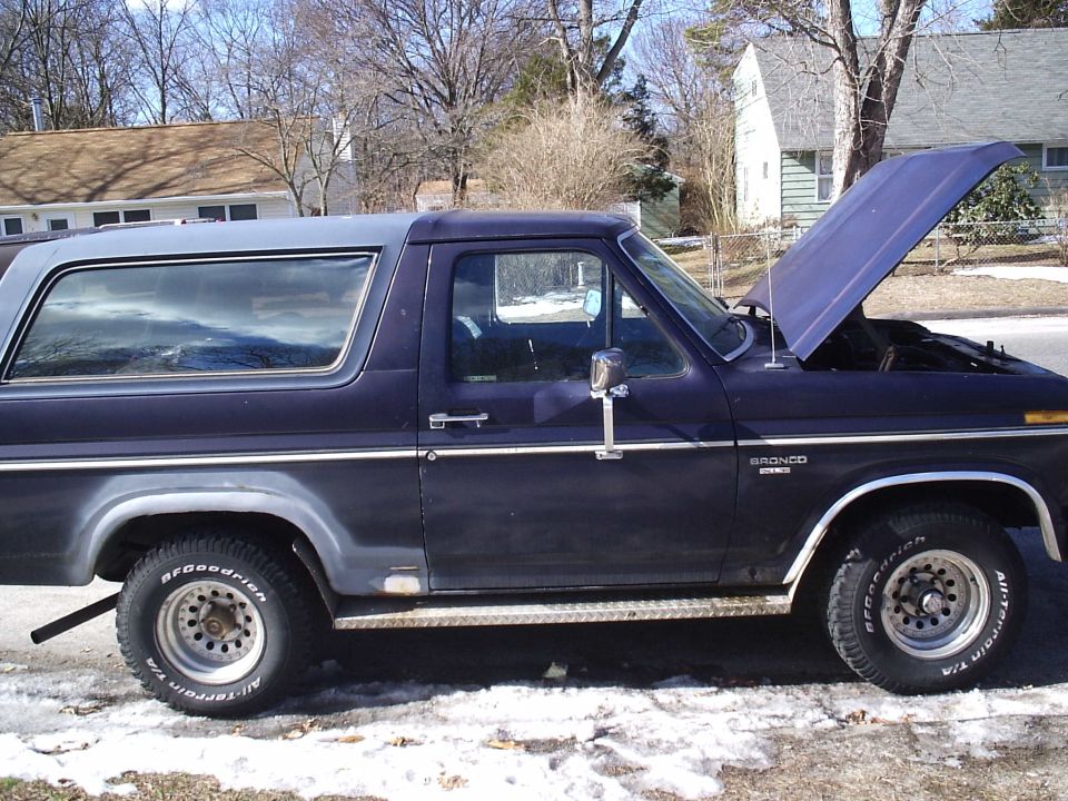 Side view of a dark blue Ford Bronco with a grey top, hood open. BFGoodrich All-Terrain T/A tires visible