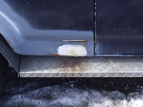1985 Ford Bronco - A close-up view of the lower body panel and step of a vehicle shows signs of rust and repair.