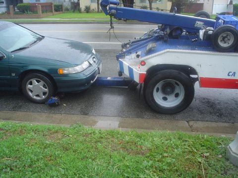 1993 Ford Taurus - A tow truck is hooking up a green sedan on a rainy day.