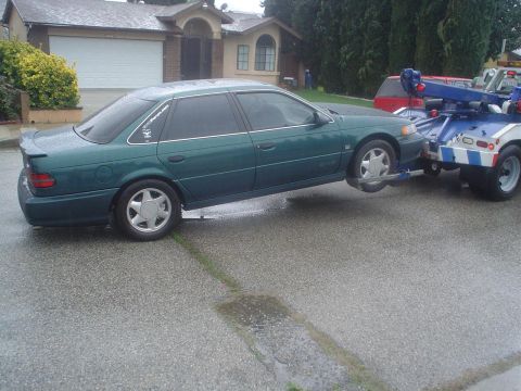 1993 Ford Taurus - A green 1993 Ford Taurus sedan is lifted onto a tow truck on a wet day.