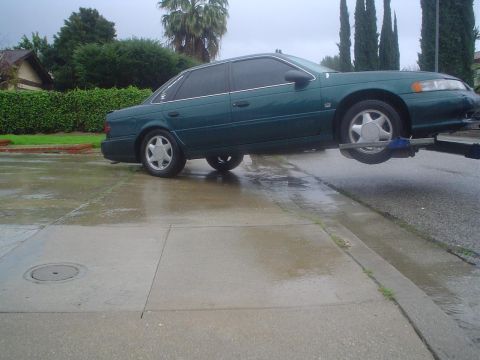 1993 Ford Taurus - A green sedan is being loaded onto a tow truck on a wet day.