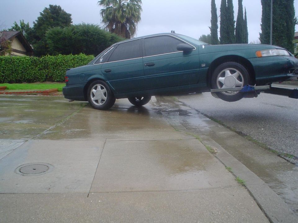 Green sedan being towed, side view. It looks like a mid-90s Ford Taurus
