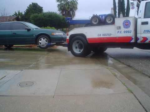 1993 Ford Taurus - A green sedan is being towed by a white tow truck on a wet day.