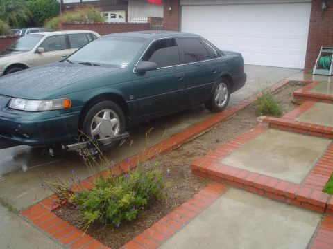 1993 Ford Taurus - A green 1993 Ford Taurus is parked in a driveway with a tow dolly attached to its front wheel.