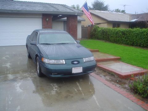 1993 Ford Taurus - Green 1993 Ford Taurus sits in a driveway on a rainy day.