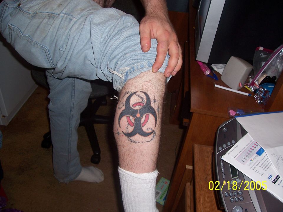 Biohazard symbol tattoo on a person's leg, with text around it