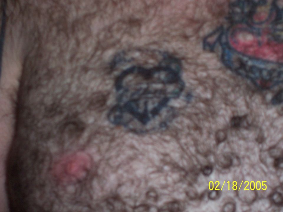 Chest tattoo of an anchor inside a heart, with other tattoo elements visible on hairy skin
