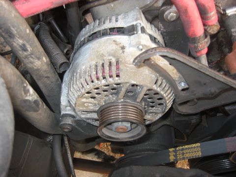1989 Ford Bronco - Close-up view of an alternator with a ribbed pulley and a visible drive belt showing text.