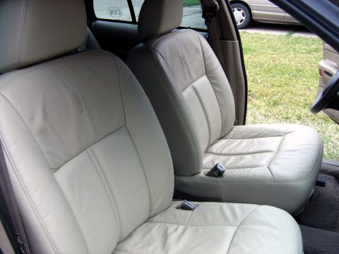 2000 Ford Crown Victoria - The interior of a car shows light tan leather seats with visible seat belts and Lincoln emblems.