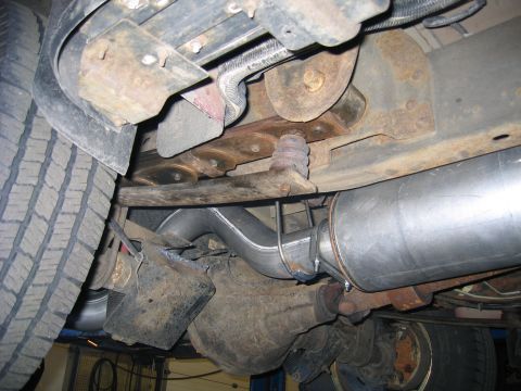 2000 Ford Excursion - The underside of a vehicle shows a new exhaust pipe connected to a muffler, with the rear axle and tire visible.