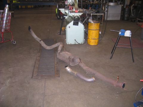 2000 Ford Excursion - A disassembled exhaust system lies on the concrete floor of a workshop, next to various machinery.