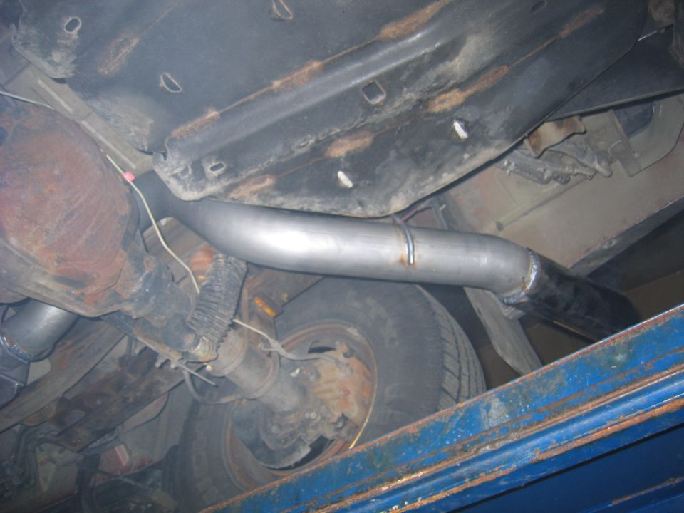 Underside view of a vehicle's exhaust pipe and rear axle. The exhaust pipe appears to be new or recently replaced