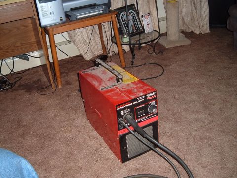 1994 Ford Bronco - A red wire feed welder is shown indoors on a carpeted floor, connected to cables.
