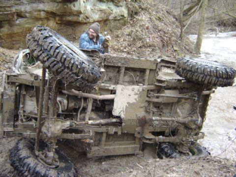 1992 Ford Bronco - An overturned off-road vehicle lies in a muddy ditch, with a person observing the scene.